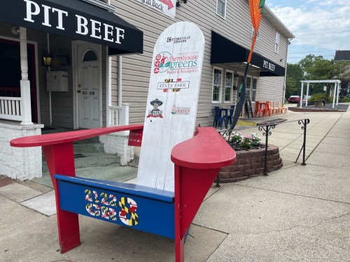 A large, colorful Adirondack chair outside a restaurant, featuring various logos and a Maryland-themed design.