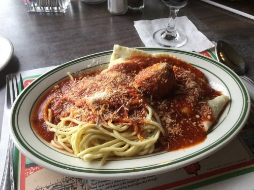 A plate of spaghetti topped with marinara sauce, a meatball, and sprinkled with grated cheese.