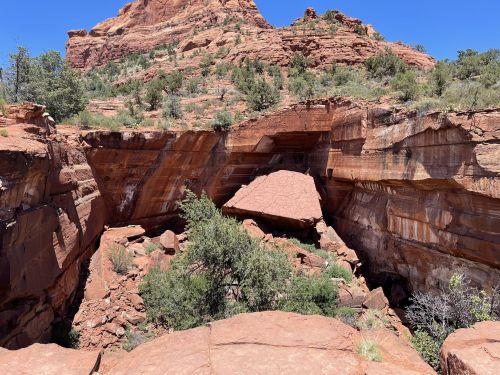 A rocky canyon with red cliffs and scattered greenery under a clear blue sky.