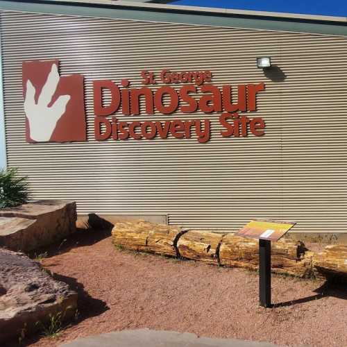 Sign for the St. George Dinosaur Discovery Site, featuring a log and landscaped area in front.