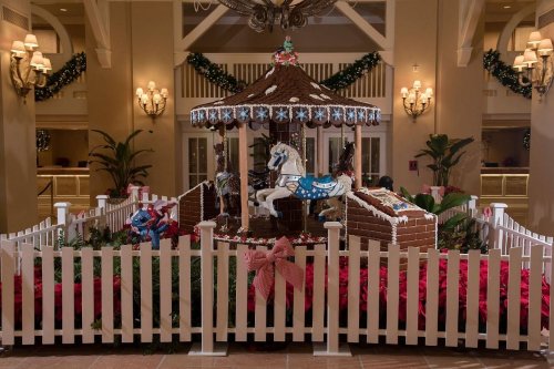 A festive gingerbread carousel with decorated horses, surrounded by a white picket fence and holiday greenery.