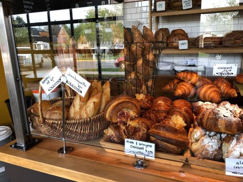 A display case filled with various baked goods, including croissants, baguettes, and pastries, with price tags visible.