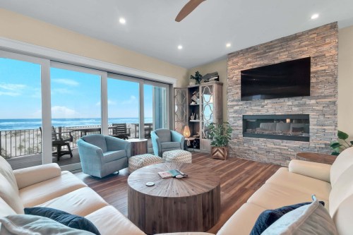 Cozy living room with a stone fireplace, large windows, and ocean views, featuring modern furniture and a round coffee table.