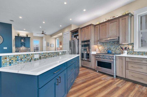 Modern kitchen with blue and wood cabinetry, marble countertops, stainless steel appliances, and colorful tile backsplash.