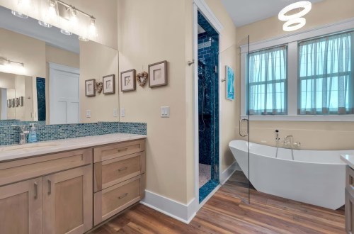Modern bathroom featuring a freestanding tub, glass shower, and blue tile accents with wooden flooring.