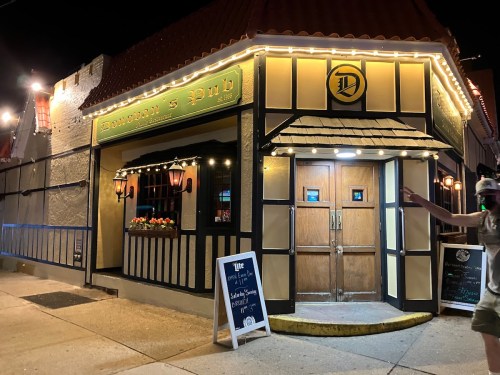A brightly lit pub at night with a welcoming entrance and decorative lights, featuring a sign that reads "Dawson's Pub."