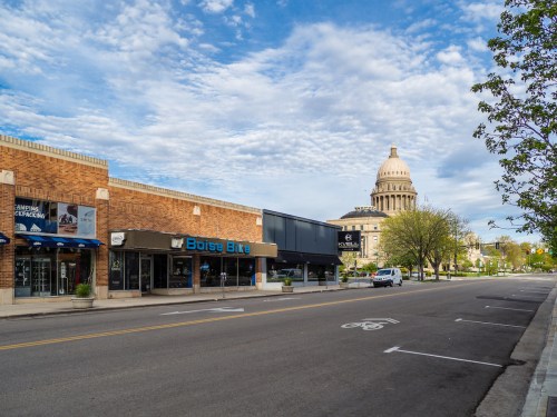 A quiet street scene featuring shops and a prominent dome building under a partly cloudy sky.