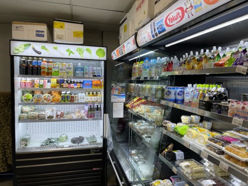 A convenience store display featuring various drinks, snacks, and packaged foods in glass-fronted refrigerators.