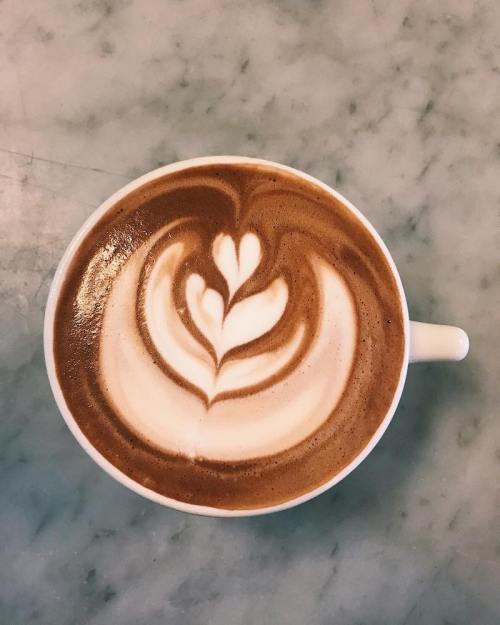 A cup of latte art featuring a heart and leaf design on a creamy surface, set on a marble table.
