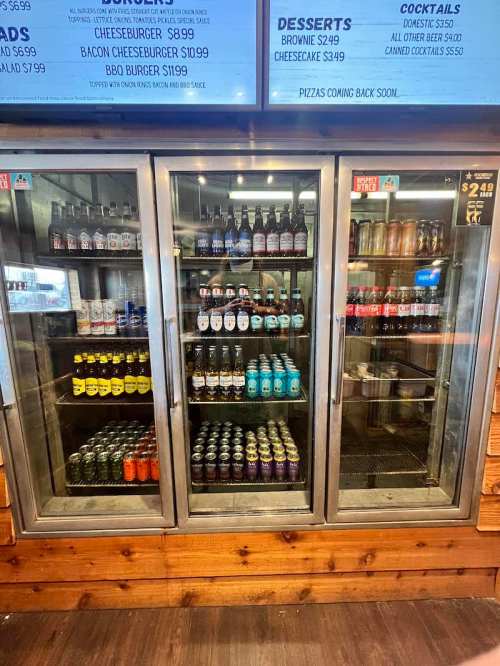 A glass-front refrigerator displaying various beverages and desserts, including sodas, beers, and desserts like brownies.