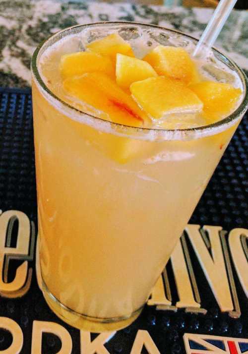 A refreshing drink in a glass, topped with ice and chunks of yellow fruit, sitting on a bar mat.