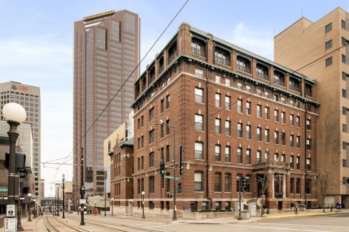 Historic brick building in the foreground with a modern skyscraper behind, set in an urban cityscape.