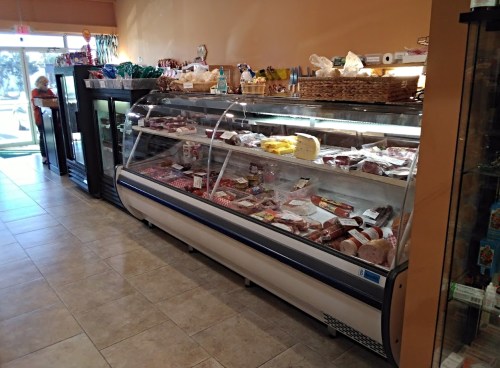 A display case filled with various meats in a grocery store, with shelves of products in the background.