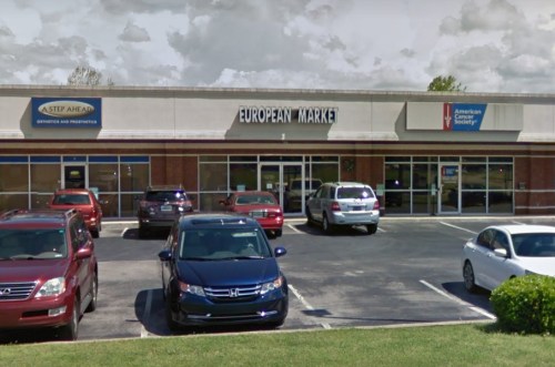 Exterior view of a shopping plaza featuring a European Market and the American Cancer Society, with parked cars in front.