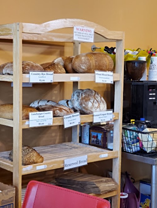 A wooden shelf displaying various types of bread with price tags, set against a warm-colored wall.