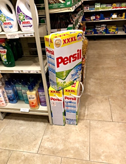 Boxes of Persil laundry detergent stacked on a store shelf, with various other cleaning products in the background.