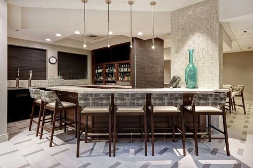 Modern bar area with high stools, a sleek counter, and a decorative vase, featuring a stylish, neutral color palette.