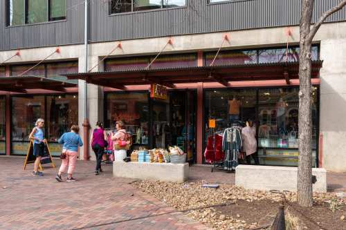 A group of people walking by a colorful storefront with clothing and accessories displayed in the windows.