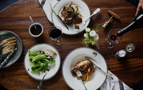A beautifully set table with gourmet dishes, including salad, roasted meat, and wine, surrounded by elegant decor.