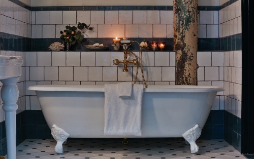A vintage bathtub with a gold faucet, surrounded by tiled walls and decorative candles, creating a cozy bathroom atmosphere.