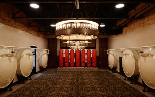 A spacious room with large white fermentation tanks, red barrels, and a decorative chandelier overhead.