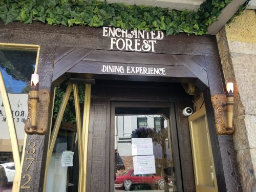 Entrance to "Enchanted Forest Dining Experience," featuring wooden decor and greenery above the door.