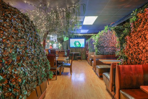 A cozy restaurant interior with greenery, soft lighting, and booths along the walls, creating a warm atmosphere.