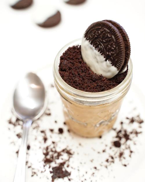 A jar of dessert layered with creamy filling and topped with crushed cookies and a whole Oreo on top.