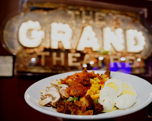A plate of food featuring chicken, mushrooms, corn, and sliced eggs in front of a vintage theater sign.