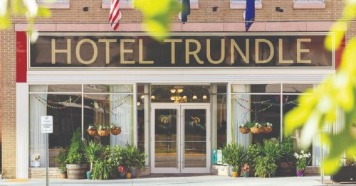 Front view of Hotel Trundle, featuring large windows, decorative plants, and a welcoming entrance.