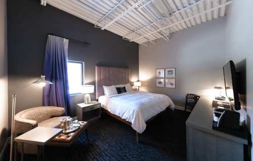 Cozy hotel room featuring a bed, armchair, desk, and modern decor with soft lighting.
