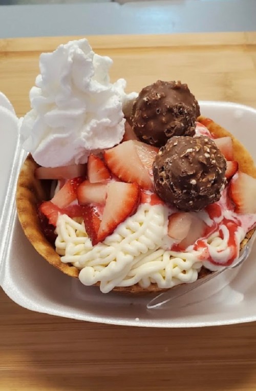 A dessert bowl with whipped cream, strawberries, chocolate balls, and a swirl of cream.