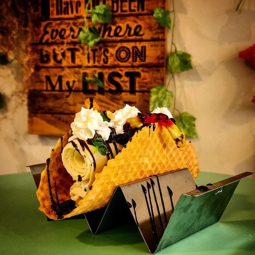 A waffle cone filled with ice cream, topped with whipped cream, chocolate drizzle, and a cherry, displayed on a stand.