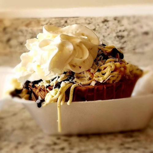 A dessert in a cup featuring a cupcake topped with whipped cream and drizzled with chocolate and caramel.