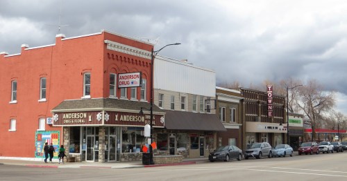 A small town street featuring a drugstore, shops, and cloudy skies overhead.
