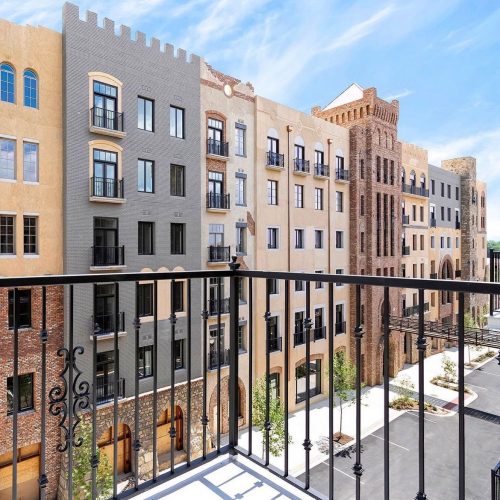 View from a balcony overlooking a modern urban building complex with a clear blue sky.