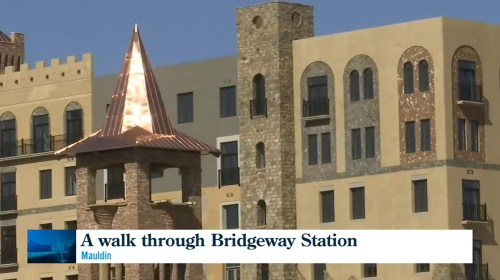 A view of Bridgeway Station featuring a tower with a copper roof and modern buildings in the background.