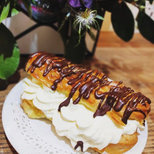 A delicious éclair topped with chocolate drizzle and filled with creamy frosting, placed on a decorative plate.