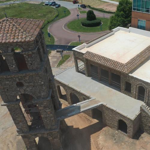 Aerial view of a stone building with a tower, surrounded by landscaping and roads under construction.