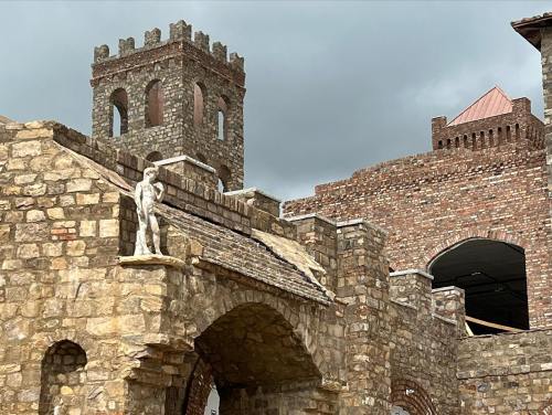 A stone castle with towers and a statue on the wall, set against a cloudy sky.