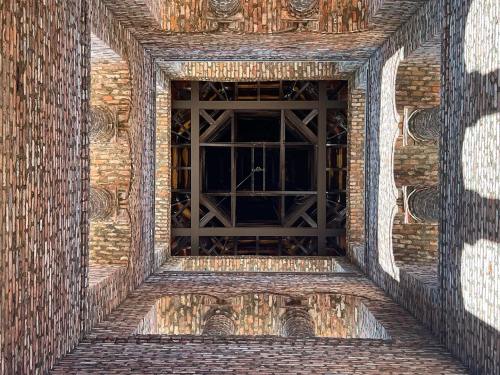 View looking up at a square brick structure with a wooden ceiling and intricate architectural details.