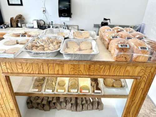 A wooden table displays various baked goods, including cookies and pastries, in clear containers and bags.