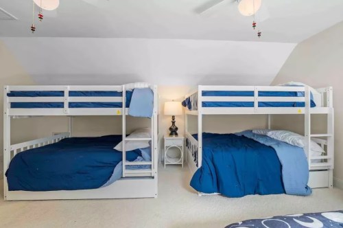 A cozy bedroom with two sets of white bunk beds, each with blue bedding, and a nightstand with a lamp in between.