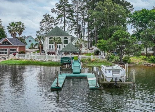 A serene waterfront scene featuring a house, dock, and lush greenery along the water's edge.