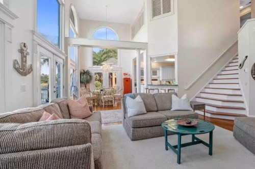 Bright, airy living room with a cozy sofa, large windows, and a staircase leading to an upper level.