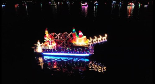 A brightly lit boat decorated with festive lights, Santa, and reindeer, floating on dark water at night.