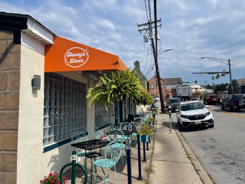 Exterior of Doozy's Diner with outdoor seating, plants, and a cloudy sky in the background.