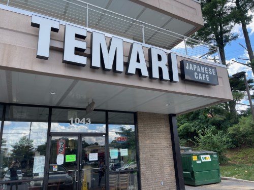 Sign for "Temari Japanese Cafe" on a building with large letters, featuring a glass entrance and outdoor seating area.