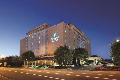 Exterior view of an Embassy Suites hotel at dusk, featuring a modern design and illuminated signage.