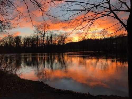 A serene river at sunset, reflecting vibrant orange and pink hues, framed by bare trees and a tranquil landscape.